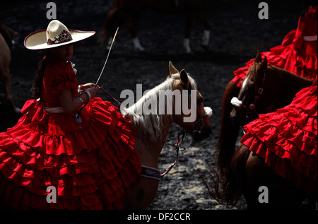 Una femmina di amazon atleta che indossa un abito rosso pratiche davanti un escaramuza fiera presso il National de Charros's lienzo,a Città del Messico Foto Stock