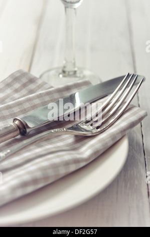 Piastra bianca, coltello e forchetta sulla luce sullo sfondo di legno.