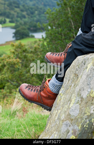 Primo piano di un uomo, un camminatore seduto a riposare su una roccia indossando stivali da passeggio Lake District National Park Inghilterra Regno Unito Regno Unito Gran Bretagna Foto Stock