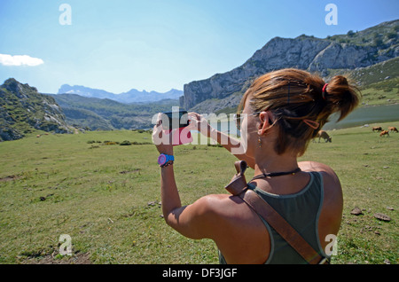 Giovane donna prende una foto dei laghi di Covadonga (Lagos de Covadonga) con il suo telefono cellulare Foto Stock