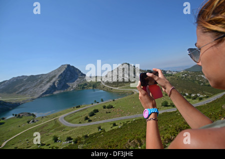 Giovane donna prende una foto dei laghi di Covadonga (Lagos de Covadonga) con il suo telefono cellulare Foto Stock