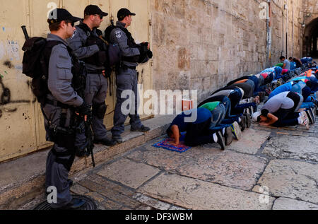 Armati di confine israeliano poliziotti di guardia accanto a quei palestinesi che sono state vietate per immettere Akza moschea e sono in preghiera nel quartiere musulmano della città vecchia di Gerusalemme il 27 settembre 2013. Le autorità israeliane hanno imposto severe restrizioni sui fedeli musulmani che vogliono eseguire venerdì la preghiera nel Santuario nobile. La polizia palestinese ha permesso agli uomini oltre 50 anno per entrare in moschea insieme con le donne e i bambini. Credito: Eddie Gerald/Alamy Live News Foto Stock