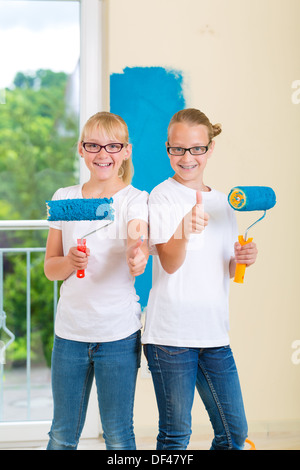 In casa famiglia ragazza con sua sorella o amico pittura con rullo di vernice di una parete in blu Foto Stock