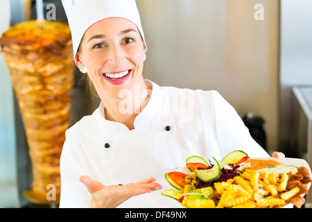 Döner Kebab - Gentile fornitore femmina in un bagno turco di fast food eatery, tenendo la piastra con le patatine fritte e kebab in parte anteriore del perno Foto Stock