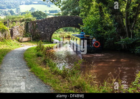 Narrowboat passa sotto il ponte di pietra sul Monmouthshire e Brecon Canal a Llangynidr nel Parco Nazionale di Brecon Beacons. Foto Stock