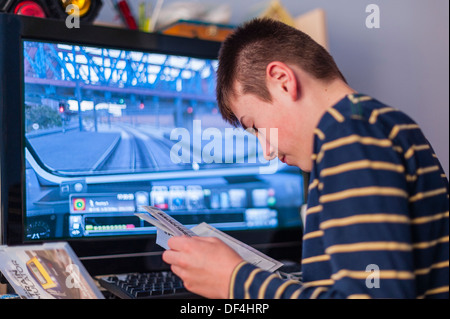 Un ragazzo di 13 anni guardando al suo computer manuale di gioco manuale di istruzioni nella sua camera da letto Foto Stock