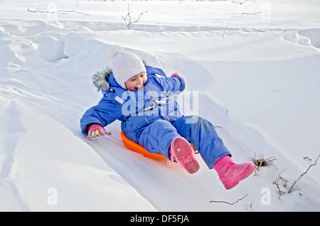 Bambina su una slitta scorrevole una discesa nella neve in inverno Foto Stock