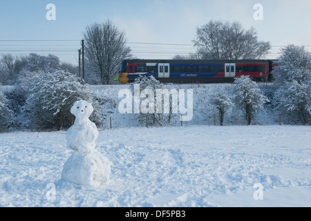 Viaggio in treno nelle fredde giornate invernali, lungo la linea ferroviaria il passante singolo pupazzo di neve in piedi in coperta di neve sul campo - Burley in Wharfedale, Inghilterra, Regno Unito. Foto Stock