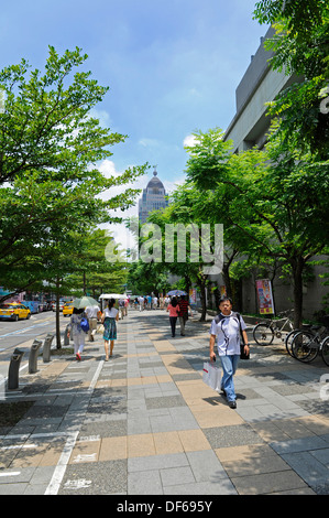 Maschio e femmina di pedoni a piedi lungo un ampio viale alberato marciapiede su un soleggiato nella città capitale di Taiwan, Taipei. Foto Stock