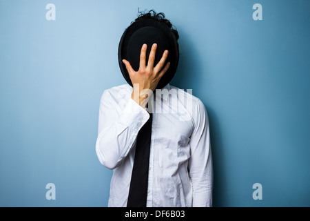 Giovane uomo nasconde la sua faccia dietro il suo cappello bowler Foto Stock