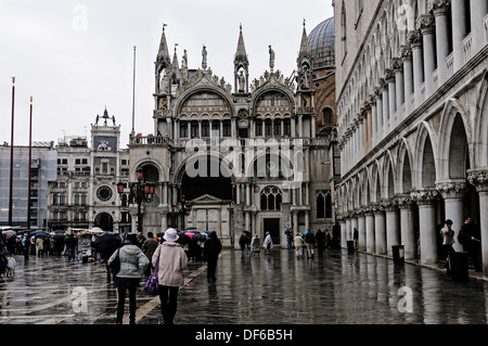 I turisti a piedi lungo il porticato Palazzo Ducale verso la facciata elegante di la Basilica di San Marco e la Torre dell'Orologio, Venezia Foto Stock