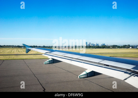 Città vista in lontananza dalla pista dell'aeroporto sopra l'ala dell'aereo Foto Stock