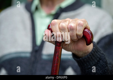 Un anziano vecchiaia titolare di pensione o di rendita si siede con le mani su un bastone da passeggio in una casa di cura. Foto Stock