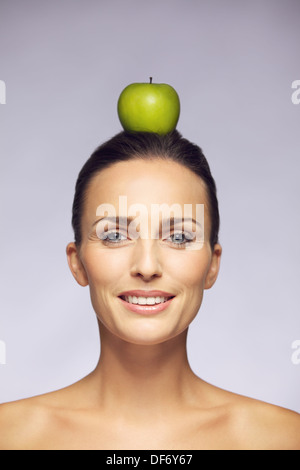 Ritratto di un bel giovane femmina il bilanciamento di una mela verde sulla testa isolata contro uno sfondo grigio. Uno stile di vita sano concetto Foto Stock