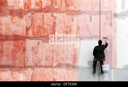 Pittore lavora sul lato esterno della parete edilizia rosso con vernice di adescamento Foto Stock