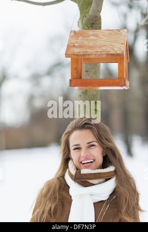 Ritratto di sorridente giovane donna in piedi sotto bird feeder in winter park Foto Stock