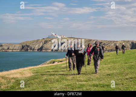 Ramblers gruppo di escursionisti a piedi su sentiero costiero con Point Lynas faro al di là in Llaneilian, Isola di Anglesey, Galles del Nord, Regno Unito, Gran Bretagna Foto Stock