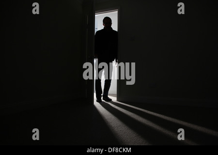 Silhouette di un maschio adulto in piedi in una porta aperta, entrando in una stanza buia. Modello rilasciato Foto Stock