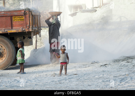 Indian i bambini giocando, circondato da polvere e non protetta, a una frantumazione della pietra opere. Andhra Pradesh, India Foto Stock