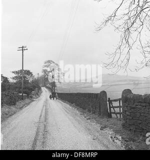 Immagine storica da anni cinquanta di una madre e bambini a piedi lungo una strada di campagna nel distretto del lago, Inghilterra. Foto Stock