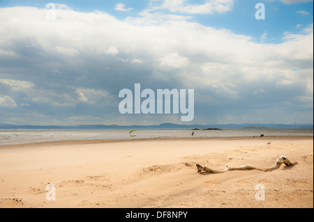 Driftwood su bruciò island beach con kite surfer cielo blu e nuvole bianche Foto Stock