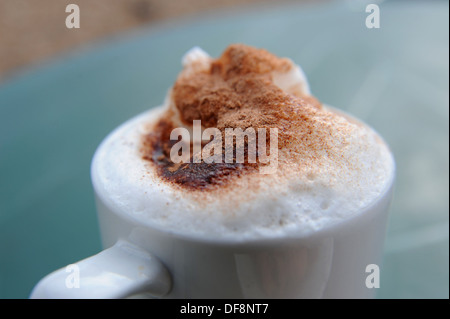 Caffè Cappuccino in una tazza e piattino con spuma di crema e cioccolato spruzza sulla parte superiore Foto Stock