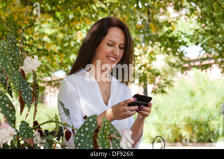Di mezza età donna caucasica utilizzando smart phone in giardino Foto Stock