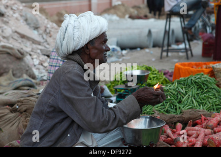 Vecchio venditore vegetali accendere una sigaretta in un mercato a Jaipur, Rajasthan,l'India. Foto Stock