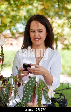 Di mezza età donna caucasica utilizzando smart phone in giardino Foto Stock