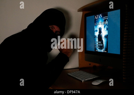 Incappucciato e uomo mascherato guardando il terrorista azan rivista on line sul suo computer Foto Stock
