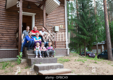 Grande famiglia caucasica con tre uomini e quattro donne e tre bambini seduti sulla veranda della casa insieme Foto Stock