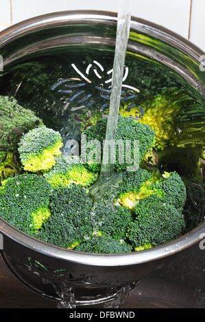 Broccoli di risciacquo in un colapasta sotto l'acqua corrente. Foto Stock