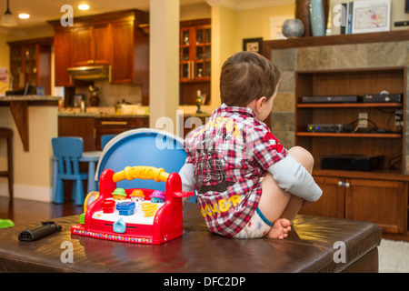 Tre anni di old boy in rosso e bianco camicia a scacchi, guardando cartoni animati in TV, seduto sulla pelle marrone otterman Foto Stock