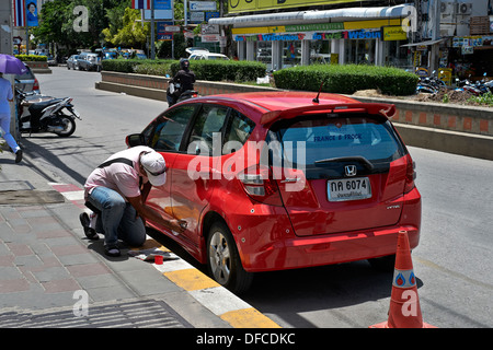 L'uomo impresa le riparazioni sul ciglio della strada e di essere nebulizzate nuovamente vernice su un rosso Honda Jazz utilizzando una bomboletta spray. Thailandia SUDEST ASIATICO Foto Stock