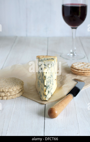 Del formaggio Stilton su di età compresa la carta pergamena con oat biscotti crackers Coltello per formaggio e un bicchiere di rosso vino di porto Foto Stock