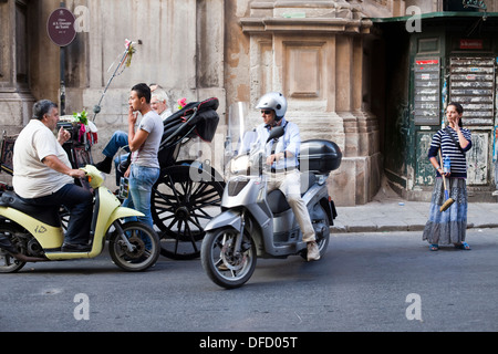 Una donna gitana attende per il lavaggio di auto mentre un uomo su uno scooter parla ai conducenti in attesa di turista per organizzare passeggiate a cavallo. Palermo Foto Stock