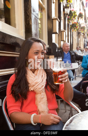 Giovane donna godendo di bere una pinta di birra in un pub, i giardinieri bracci, Norwich, Norfolk, Inghilterra, Regno Unito Foto Stock