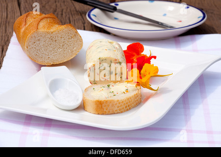 In casa nasturtium burro alle erbe su una piastra con un pezzo di baguette e sale di mare su una tavola in legno rustico Foto Stock