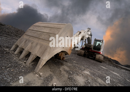 Ampio angolo di immagine di un escavatore in una cava con un drammatico sfondo cielo. Focus sulla pala in primo piano. Foto Stock