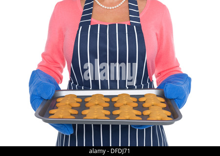 Una donna che indossa un grembiule di cottura tenendo un vassoio di pane appena sfornato gingerbread uomini Foto Stock