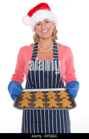 Una donna che indossa un cappello da Babbo Natale e grembiule tenendo un vassoio di pane appena sfornato gingerbread uomini, isolata su uno sfondo bianco. Foto Stock