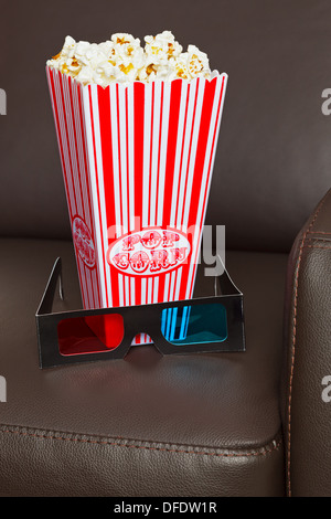 Scatola di popcorn con Occhiali TV 3D su una pelle marrone home cinema sedia. Foto Stock