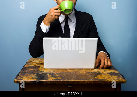 Giovane imprenditore è di bere il caffè e il lavoro sul suo portatile a una vecchia scrivania Foto Stock