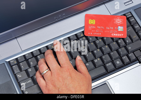 Una donna la digitazione in lei i dettagli della carta di credito su un computer portatile. La carta è un mock-up fatta da me. Foto Stock