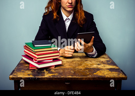 Giovane imprenditrice è seduta su una vecchia scrivania con una pila di libri e lettura su una tavoletta digitale Foto Stock