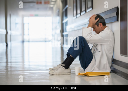 Medico seduto sul pavimento nel corridoio di ospedale con testa in mani Foto Stock