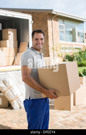 Ritratto di uomo sorridente tenendo la scatola di cartone vicino a spostamento van nel viale di accesso Foto Stock