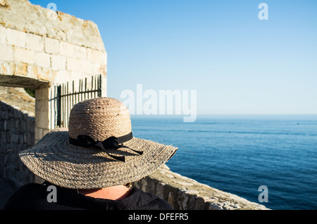 Una donna che indossa un cappello per il sole si affaccia al mare dalle mura della città nella città vecchia di Dubrovnik, Croazia. Foto Stock