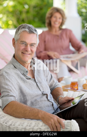 Senior uomo con tavoletta digitale in poltrona sul patio Foto Stock