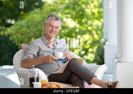 Ritratto di sorridente uomo senior di bere il caffè sul patio Foto Stock
